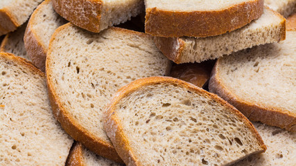 Brown bread pile detail. Half slices as side dish portions. Staple food. Culinary background from many slabs of sliced crunchy loaf. Rustic texture of salty baked product from wheat flour with crust.