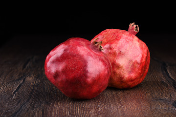 Two ripe pomegranates on a wooden table and dark background.