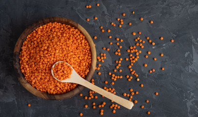 Red raw organic bio lentils in a wooden bowl with a wooden spoon stuck in it on a dark background....