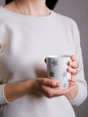 The girl in a cozy clothes drinking coffee froma a mug. hands holding hot cup of coffee or tea in morning. cup in female hands