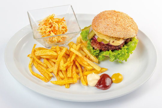 fast food menu. hamburger, french fries and salad. burger with beef stake, cheese onion and pickle. mayonnaise ketchup mustard on the white plate. healthy variation of junk food