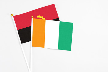 Cote D'Ivoire and Angola stick flags on white background. High quality fabric, miniature national flag. Peaceful global concept.White floor for copy space.