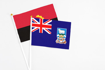 Fototapeta premium Falkland Islands and Angola stick flags on white background. High quality fabric, miniature national flag. Peaceful global concept.White floor for copy space.