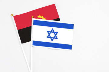 Israel and Angola stick flags on white background. High quality fabric, miniature national flag. Peaceful global concept.White floor for copy space.