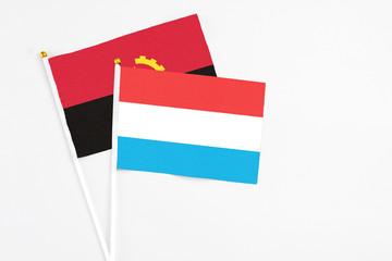 Luxembourg and Angola stick flags on white background. High quality fabric, miniature national flag. Peaceful global concept.White floor for copy space.