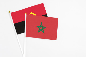 Morocco and Angola stick flags on white background. High quality fabric, miniature national flag. Peaceful global concept.White floor for copy space.
