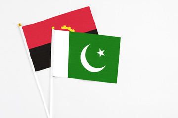 Pakistan and Angola stick flags on white background. High quality fabric, miniature national flag. Peaceful global concept.White floor for copy space.