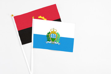 San Marino and Angola stick flags on white background. High quality fabric, miniature national flag. Peaceful global concept.White floor for copy space.