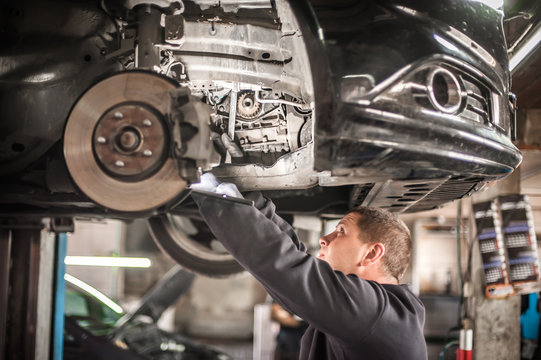 Auto Mechanic Repairer Checking Condition Under Car On Vehicle Lift