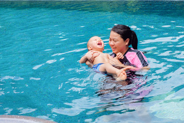 Smiling Asian mother & Cute little Asian 1 year old / 18 months toddler boy child relaxing playing in the swimming pool outdoor on nature, Mom and baby enjoying summer vacation at a tropical resort