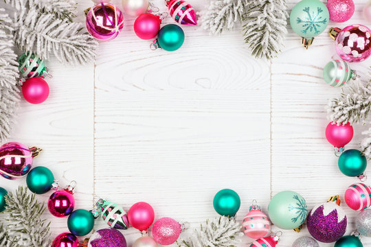 Christmas frame with pink, purple and teal baubles and tree branches. Top view on a white wood background.