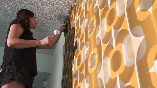 Real woman improving, renovating and decorating her home by hanging 1970's retro wallpaper