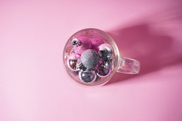 Pink and gray christmas balls in a transparent glass cup, on a pink background