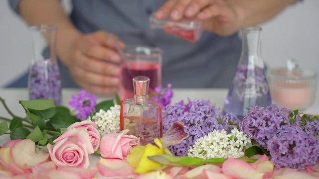 Making body care production beauty aroma perfume lilac iris roses flowers background, Hand of male perfumer lab technician chemist cosmetician pouring cosmetic aroma glass test tube oil in liquid, 4 K