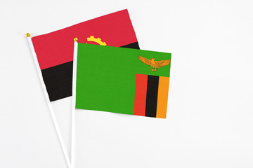 Fototapeta premium Zambia and Angola stick flags on white background. High quality fabric, miniature national flag. Peaceful global concept.White floor for copy space.