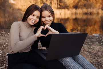 Attractive two young twin sisters in casual outfit with bright smile use notebook or laptop at the park