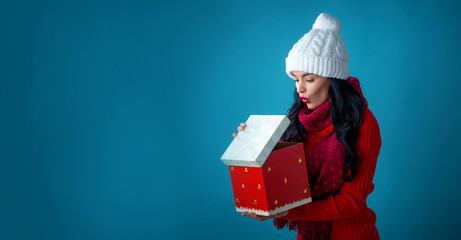Young woman with santa hat opening a Christmas gift box on a dark blue background