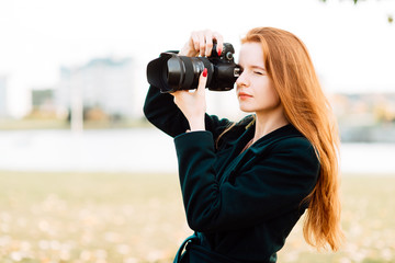 portrait of cute cheerful young girl with amazing red hair posing outdoors holding camera, redhead woman is relaxing on the park