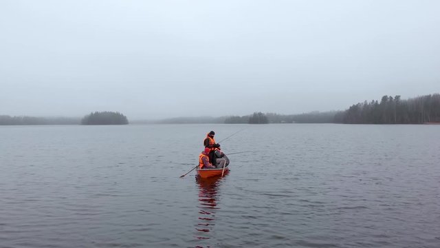 Three men in orange boat fishing on lake in Finland in fog static