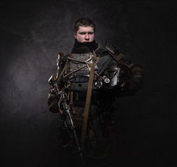 Portrait of young serious man in doomsday warrior's costume at dark photo studio.