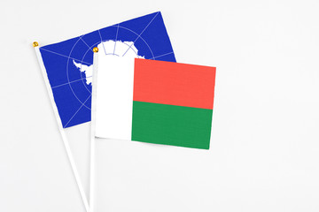 Madagascar and Antarctica stick flags on white background. High quality fabric, miniature national flag. Peaceful global concept.White floor for copy space.