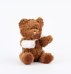 brown teddy bear with rewound white bandage paw on a white background