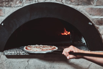 Italian chef is putting prepared margarita pizza to the oven with flame in it.