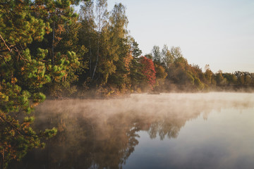 Morning calm lake with mist and reflection of forest on bright autumn day.