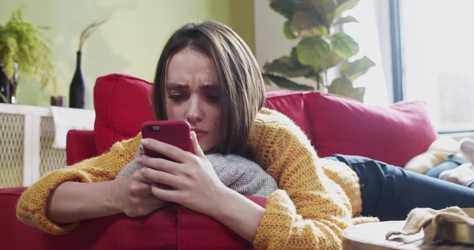 Beautiful relaxed girl lyng on comfort couch using smartphone content. Close-up unhealthy woman sneezing allergy having cold staying at home.