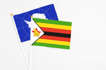 Zimbabwe and Antarctica stick flags on white background. High quality fabric, miniature national flag. Peaceful global concept.White floor for copy space.