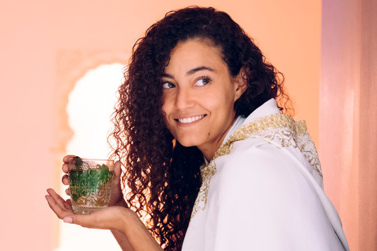 Portrait of beautiful ethnic marrakech woman holding arab tea. Arabian culture and traditions. Moroccan green herbal tea poured in traditional ways. Healthy beverage. Muslim lifestyle at home.