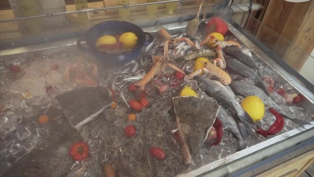 Mixed seafood: mussels, gobies, flounder, king prawns on an ice counter in a restaurant kitchen.