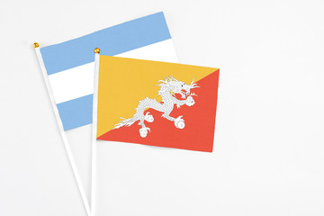 Bhutan and Argentina stick flags on white background. High quality fabric, miniature national flag. Peaceful global concept.White floor for copy space.