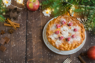 Delicious Christmas raspberry pie with berry filling and icing sugar and spices on a dark rustic background.