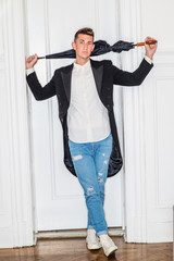 Young Man Fashion in New York City. 20 years old man wearing black Swallow - Tailed coat, white shirt, blue ripped Denim jeans, sneakers, sunglasses, carrying black stick umbrella with hook handle, .