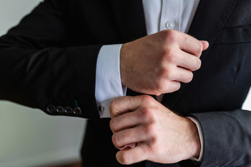 Obraz premium Businessman in an expensive black suit fixes cufflinks on his white shirt. A man in a classic suit adjusts the cuffs of his shirt. Successful business concept