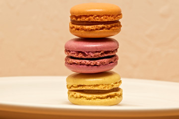 Three small colorful french macaron cookies of different colors and flavors on white plate or dish.