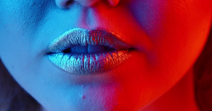 Close up shot of lips of a young girl with glowing makeup making a beautiful positive sensual smile in neon light - emotions, nightlife concept 4k footage