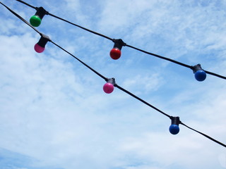 Closeup of many round bulb hanging on a black wire On the blue sky background with white clouds With copy space