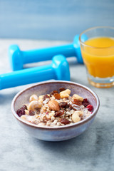 Bowl of granola with yogurt, nuts, raisins, cranberries and chia seeds. Blue dumbbells in background. Concept for a tasty and healthy meal. Stone - wooden background. Close up.
