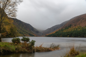 Long exposuire view, silky water during autumn in the Wicklow Mountains. Rock on front, Glendalough Upper lake covered with mist and fog in upper part, calm water, view from low angle