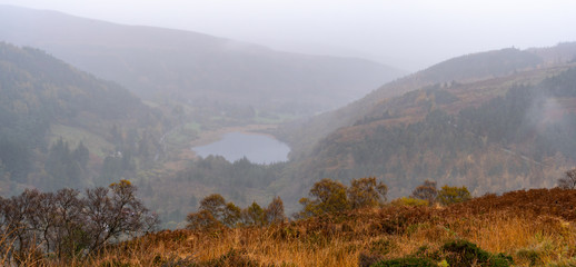 Panoramic view for Glendalough Lower lake from the top of Glenealo valley, Wicklow way, County Wicklow, Ireland. Autumn hike during foggy weather and mist.