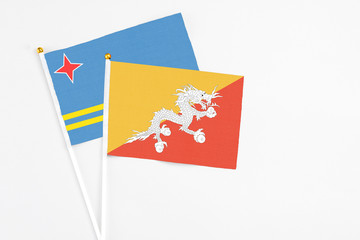 Bhutan and Aruba stick flags on white background. High quality fabric, miniature national flag. Peaceful global concept.White floor for copy space.