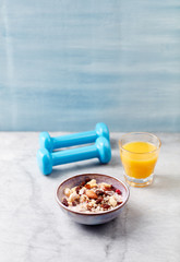 Bowl of granola with yogurt, nuts, raisins, cranberries and chia seeds. Blue dumbbells in background. Concept for a tasty and healthy meal. Stone - wooden background. Copy space.