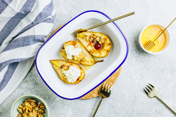 Sweet baked pears with honey, nuts, cranberries and cinnamon in enameled baking bowl on stone background. Top view. Flat lay