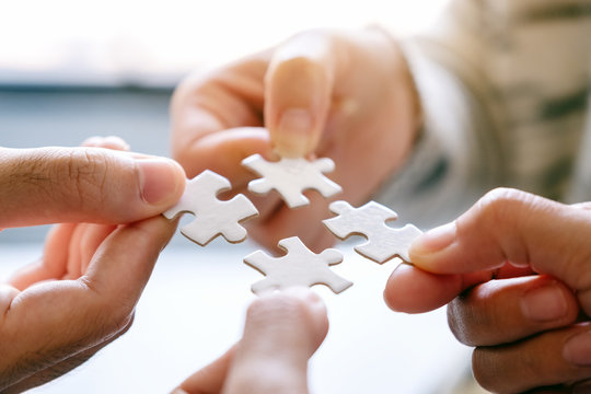 Closeup image of many people holding and putting a piece of white jigsaw puzzle together