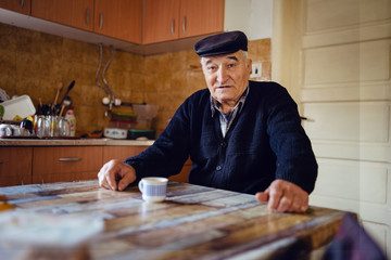 Senior man grandfather old pensioner farmer wearing black sweater and hat having a cup of coffee or...