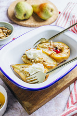 Sweet baked pears with honey, nuts, cranberries and cinnamon in enameled baking bowl on stone background. Top view. Flat lay