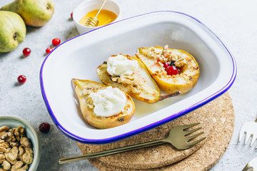 Sweet baked pears with honey, nuts, cranberries and cinnamon in enameled baking bowl on stone background. Top view. Flat lay