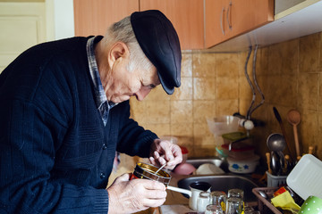 Senior man grandfather old pensioner farmer wearing black sweater and hat making a cup of coffee or tea cooking in the pot at home putting coffee to the pot with spoon